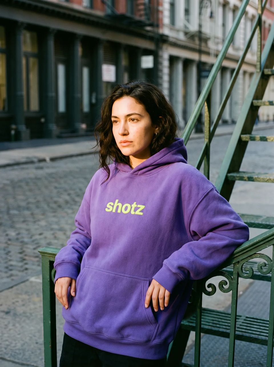 Violet hoodie with a large lime shotz wordmark, worn on a SoHo stoop at golden hour
