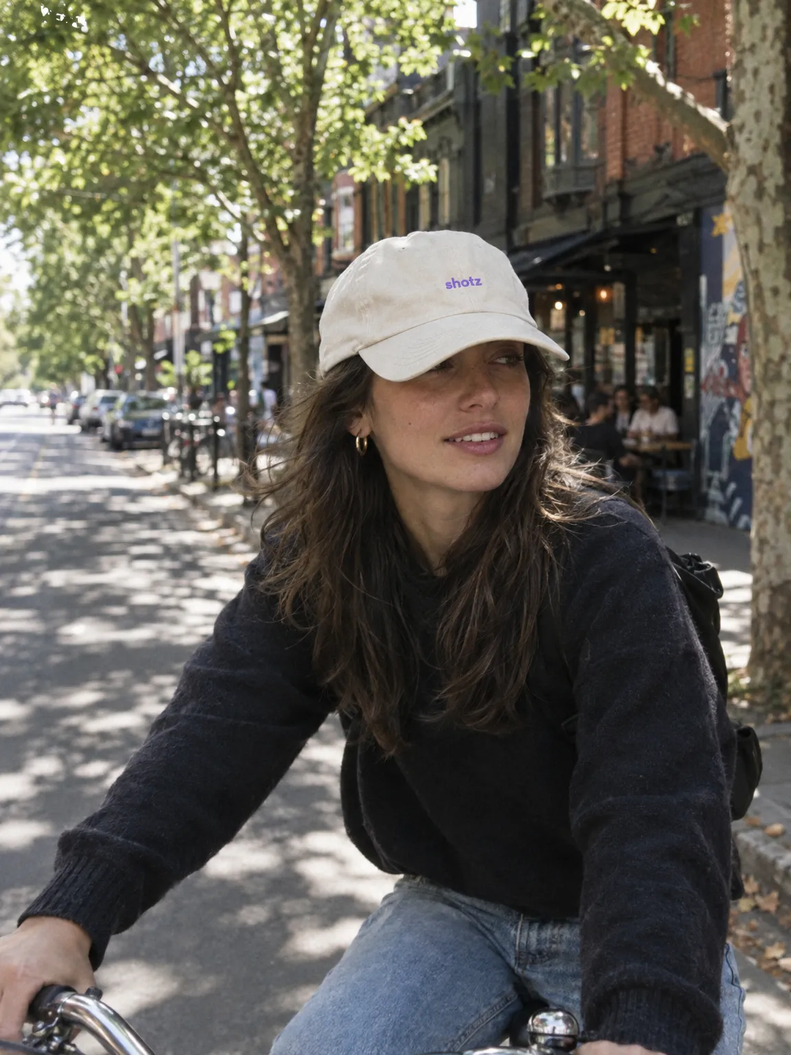 Bone dad cap with a small violet shotz embroidery, worn riding a bike down a leafy street