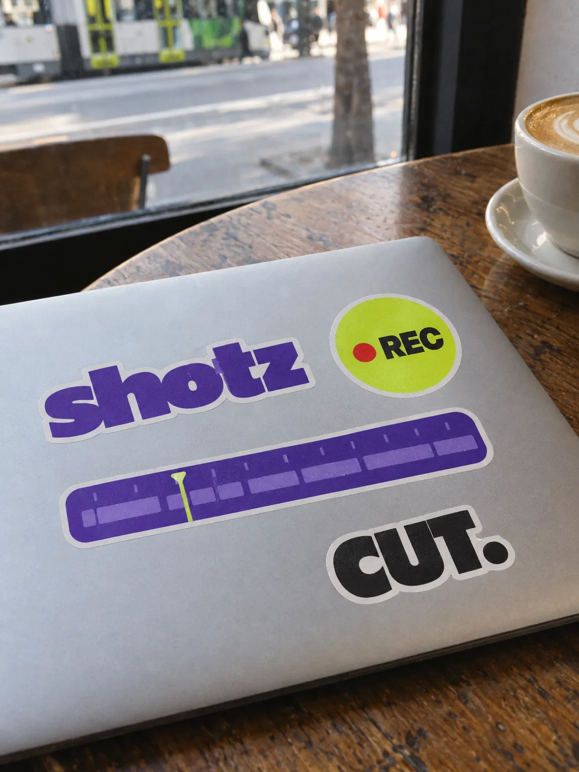 Die-cut stickers on a laptop lid: the shotz wordmark, a lime REC dot, a violet timeline and CUT.