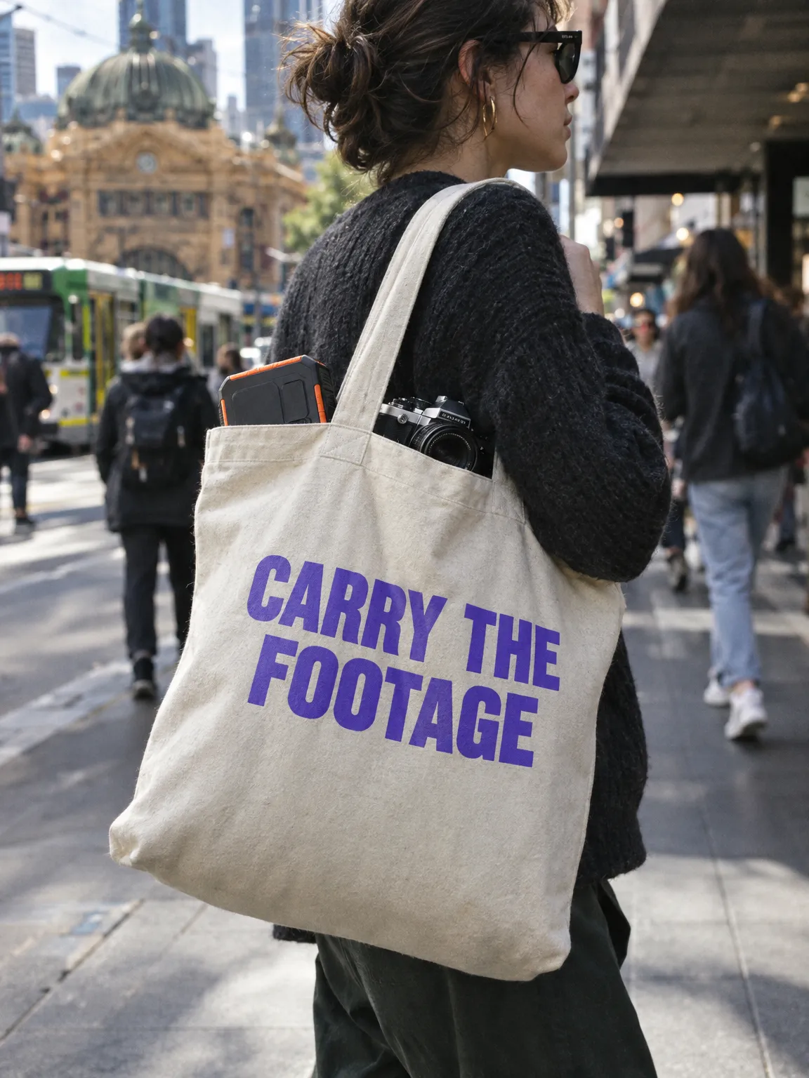 Canvas tote printed CARRY THE FOOTAGE in violet, carried past Flinders Street Station